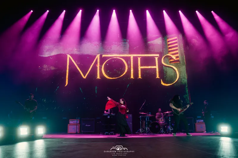 MOTHS on stage with dramatic lighting and logo backdrop